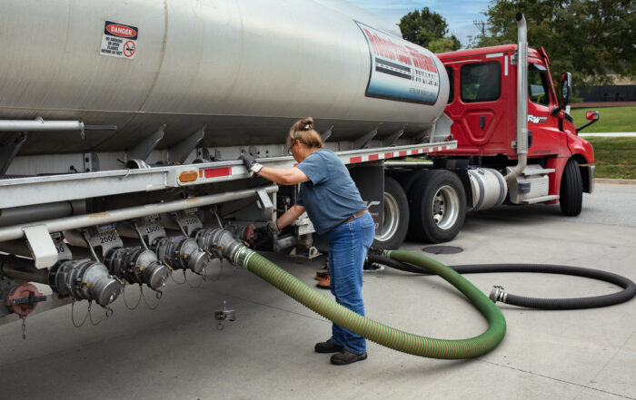 Robertson-Williams Transport driver connecting a delivery hose to a bulk fuel tanker trailer during a scheduled fuel delivery